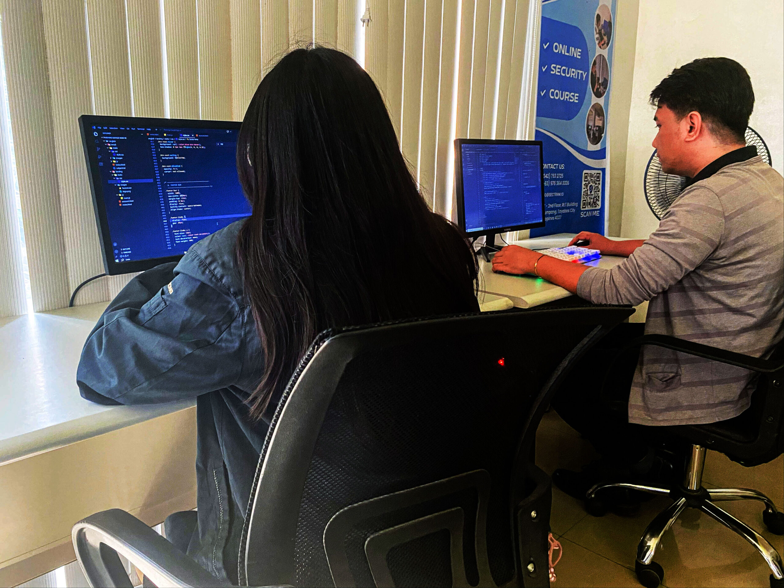 Two individuals working on coding tasks at their desks using computers.